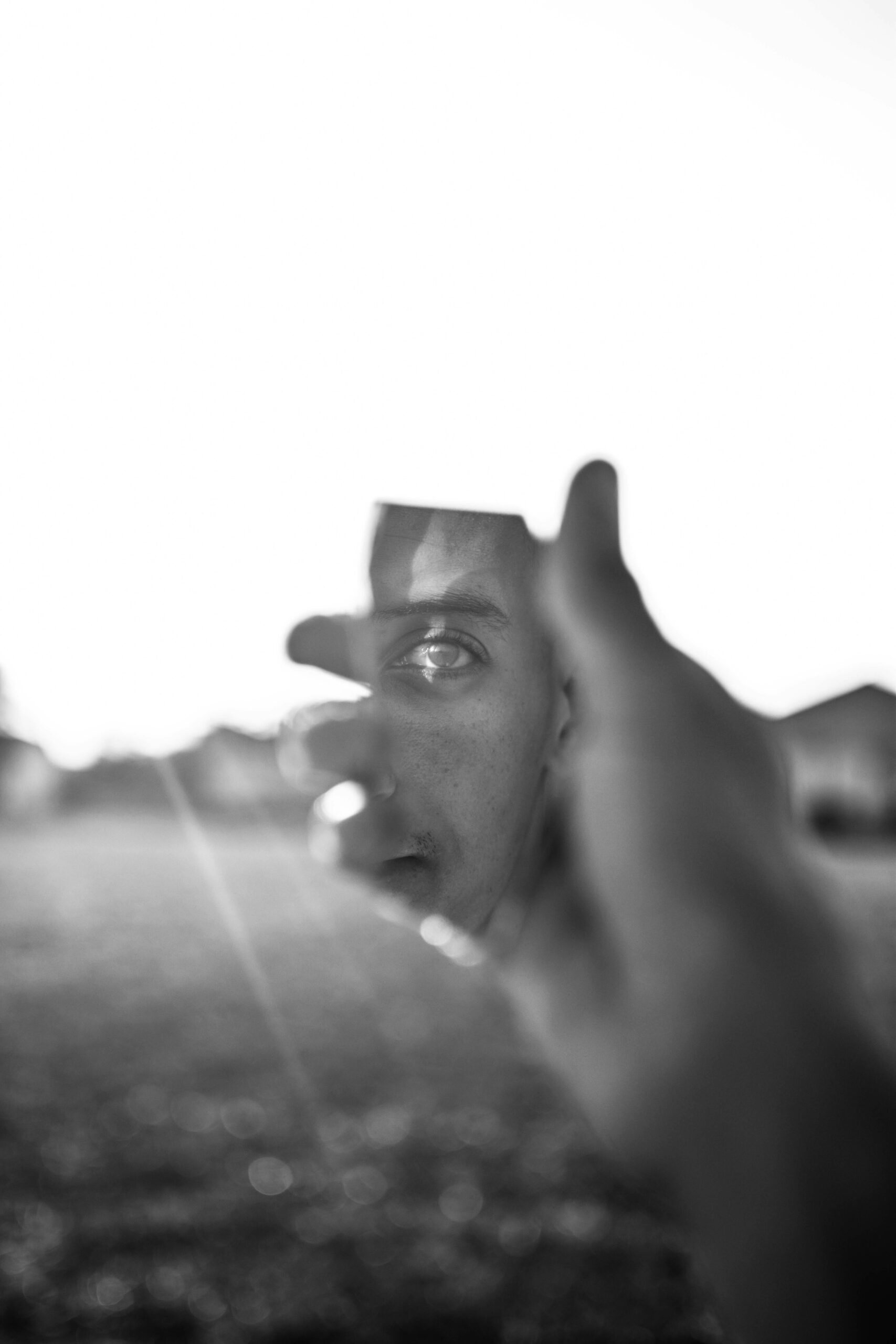 Creative black and white portrait featuring a man's reflection in a broken mirror piece, held by a hand.